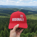 Aus der Ich-Perspektive hält eine Hand eine rote Kappe mit dem "REGIONAL STAR"- und "Rewe"-Logo in den Vordergrund. Im Hintergrund erstreckt sich eine weite, malerische Landschaft aus dichten Wäldern und sanften Hügeln.