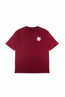 Die Vorderseite eines weinroten Unisex-T-Shirts in der Frontalansicht auf weißem Hintergrund. Das Shirt ist schlicht gehalten und zeigt lediglich ein kleines, einzelnes weißes Gänseblümchen als Akzent auf der linken Brustseite.