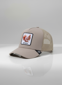 Ein professionelles Produktfoto einer beigen Trucker-Kappe. Auf der Vorderseite befindet sich ein quadratischer Aufnäher, der ein Eichhörnchen und den Schriftzug "OACHKATZL" zeigt. Die Kappe steht auf einer spiegelnden Oberfläche vor einem hellen Studiohintergrund, was eine deutliche Reflexion erzeugt.