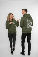Ein Paar, ein Mann und eine Frau, posiert in passenden olivgrünen Kapuzenpullovern vor einem hellgrauen Hintergrund. Der Mann steht mit dem Rücken zur Kamera und präsentiert den großen "Goassmass"-Aufdruck, während die Frau lachend mit beiden Zeigefingern auf seinen Rücken zeigt.