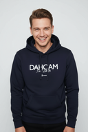 Ein junger Mann mit einem breiten, freundlichen Lächeln blickt direkt in die Kamera. Er trägt einen dunkelblauen Kapuzenpullover mit der weißen Aufschrift "DAHOAM".