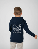 Ein kleiner Junge, von hinten fotografiert, präsentiert den großen weißen Aufdruck auf seinem dunkelblauen Kapuzenpullover, der einen Traktor und den Schriftzug "OIS GEHT O MIT AM TRAUM" zeigt.