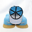 Ein Produktfoto von drei "Ois Easy"-Kappen, das verschiedene Details zeigt. Während zwei Kappen im Vordergrund die Vorderseite präsentieren, ist die Kappe in der Mitte umgedreht, um die gemusterte Unterseite des Schirms im Rauten-Design und das Innere mit dem Snapback-Verschluss zu zeigen.