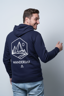Ein Mann, von der Seite von hinten fotografiert, präsentiert den großen weißen "WANDERLUST"-Aufdruck auf seinem dunkelblauen Kapuzenpullover. Er blickt mit einem breiten, fröhlichen Lächeln über die Schulter.