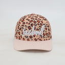 Ein professionelles Produktfoto einer Kinder-Kappe in der Vorderansicht vor einem weißen Hintergrund. Die Kappe hat ein Leopardenmuster, einen rosa-weiß gestreiften Schirm und den weißen, kursiven Schriftzug "Lausdeandl" auf der Vorderseite.

