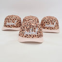 Ein Produktfoto von vier identischen Kinder-Kappen, die auf einer weißen Fläche arrangiert sind. Jede Kappe kombiniert ein Leopardenmuster mit einem gestreiften Schirm und hat den weißen, kursiven Schriftzug "Lausdeandl" auf der Vorderseite.