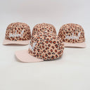 Vier identische Kinder-Kappen, die aus einer seitlichen Perspektive fotografiert wurden. Jede Kappe zeigt die Kombination aus Leopardenmuster auf der Kappe und einem rosa-weiß gestreiften Schirm vor einem weißen Studiohintergrund.