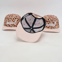 Ein Produktfoto von drei Kinder-Kappen mit "Lausdeandl"-Schriftzug, das verschiedene Details zeigt. Während zwei Kappen im Hintergrund die Vorderseite mit Leopardenmuster präsentieren, ist die Kappe in der Mitte umgedreht, um die gestreifte Unterseite des Schirms und das Innere zu zeigen.